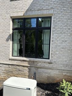 a white refrigerator sitting in front of a brick building next to a tree and bushes