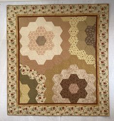 a close up of a patchwork quilt on a white wall with brown and tan colors