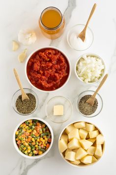 bowls filled with different types of food on top of a white counter next to wooden spoons