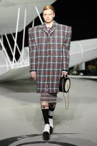 a man walking down a runway wearing a plaid coat