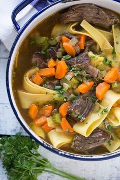 a bowl of beef noodle soup with carrots and parsley