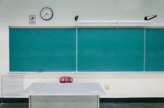 an empty desk in front of a chalkboard with a clock on the wall behind it