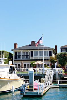 the boat is docked at the dock in front of the large house with an american flag on it's roof