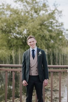 a man in a suit and tie standing on a bridge next to a body of water