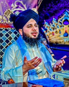 a man sitting at a table with a microphone in his hand and wearing a turban