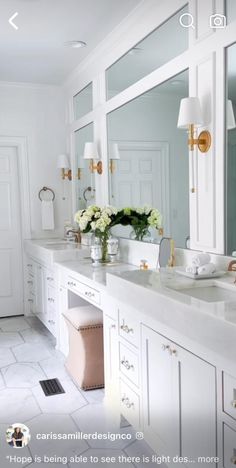 a white bathroom with two sinks and large mirrors on the wall, along with flowers in vases