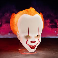 a close up of a creepy clown mask on a table with red and orange lights