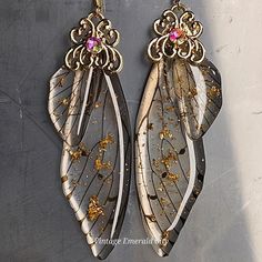 two pairs of gold and silver earrings with pink stones on them, hanging from hooks