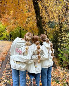 three girls in white jackets are walking down the street with their arms around each other