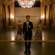 a man in a tuxedo taking a selfie with two other women and a chandelier