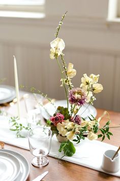 the table is set with white plates and silverware, flowers in a vase on top