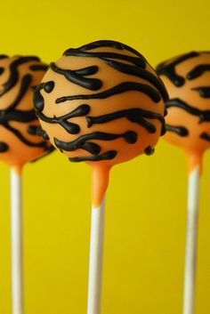 three cake pops with chocolate and orange frosting on top, lined up against a yellow background