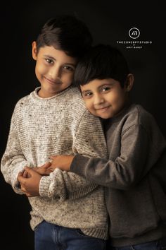 two young boys hugging each other in front of a black background