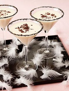 three martini glasses filled with white wine and garnished with chocolate on a black tray