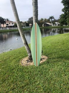 a green surfboard sitting on top of a lush green field next to palm trees