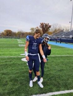 two football players are standing on the field with their helmets in hand and one is holding his arm around the other's shoulder