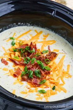 a black crock pot filled with cheese, bacon and sour cream soup garnished with green onions