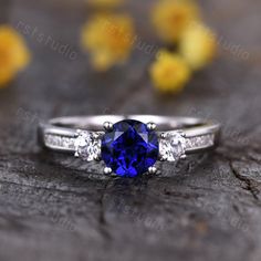 a blue sapphire and diamond ring sitting on top of a piece of wood with yellow flowers in the background