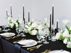 the table is set with black linens and white flowers, gold cutlery, and candles