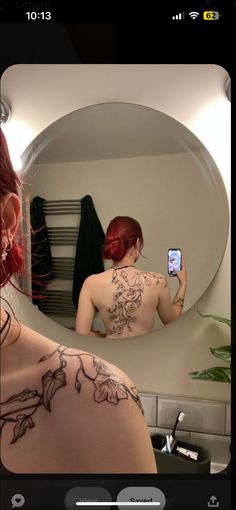 a woman taking a selfie in front of a mirror with tattoos on her back