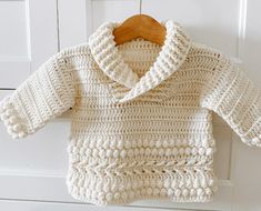 a crocheted sweater hanging on a wooden hanger in front of a white door