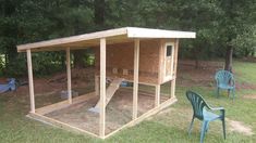 a chicken coop in the middle of a yard with chairs around it and trees behind it