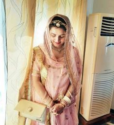 a woman in a pink sari is holding a white purse and standing next to an air conditioner