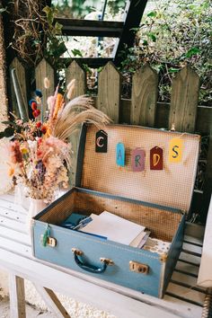 an open suitcase sitting on top of a wooden bench next to a plant and flowers