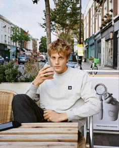 a man sitting on a wooden bench next to a tree and holding a cell phone