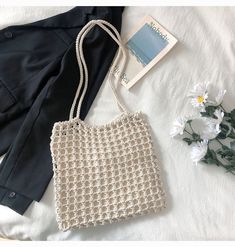 a white crocheted bag sitting on top of a bed next to a book