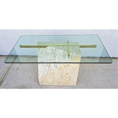 a glass table with a piece of wood in the middle on concrete floor next to white wall