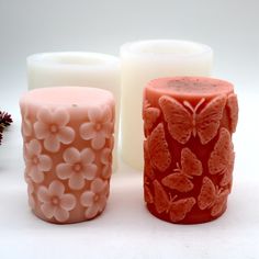 three candles sitting next to each other on a white surface with flowers and butterflies carved on them