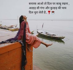 a woman sitting on the edge of a wall next to water with boats in the background