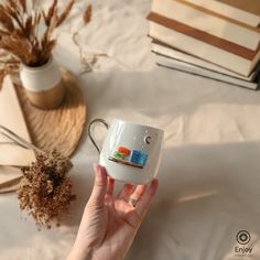 a hand holding a coffee mug with an orange and blue sticker on it next to some books