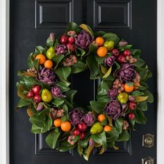 a wreath is hanging on the front door with fruit and leaves around it, as well as flowers