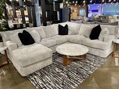 a large sectional couch with black and white pillows in a furniture showroom, next to a round coffee table