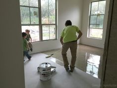 a man in a green shirt is painting the floor with two children looking out the window