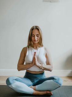 a woman is sitting in the middle of a yoga pose with her hands together and eyes closed