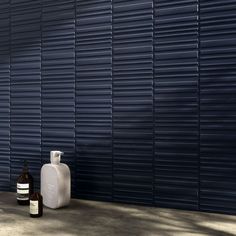 two bottles of wine sitting next to each other near a wall with vertical slats on it