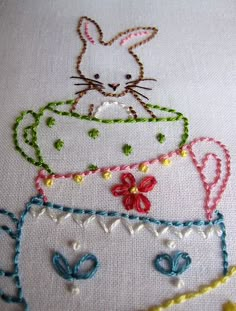 a close up of a cross stitch pattern on a piece of cloth with a cat in a cup