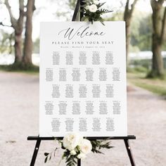 a welcome sign with white flowers and greenery sits on top of a black easer