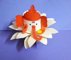 an origami elephant head on top of a white flower with orange ears and tail