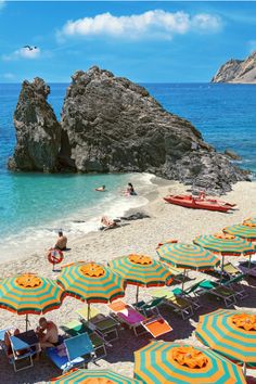 many umbrellas and chairs on the beach with people in the water near large rocks