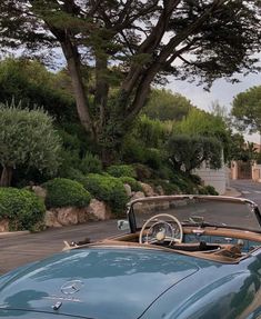 an old blue convertible car parked on the side of a road next to a tree