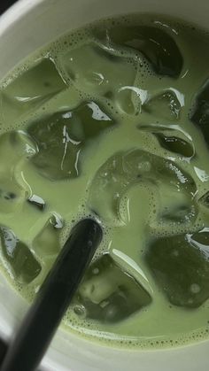 a white bowl filled with green liquid next to a black ladle on top of a table