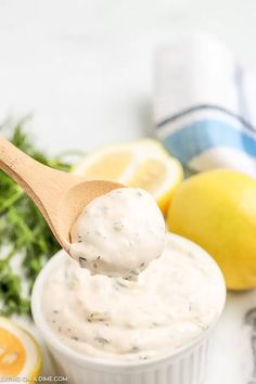 a wooden spoon full of white sauce next to lemons