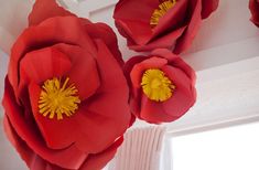 three red paper flowers are hanging from the ceiling in front of a white window sill