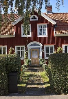 a red house with white trim on the front door and windows, surrounded by hedges