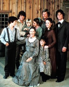 a group of people standing next to each other in front of a wooden building and fence