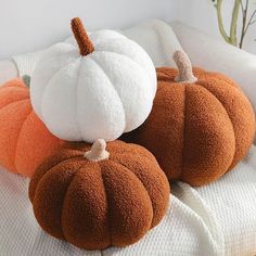 three pumpkins sitting on top of a white bed next to a potted plant